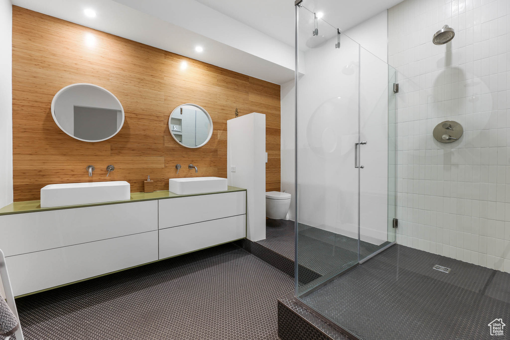 Bathroom featuring a shower stall, double vanity, toilet, wood walls, and recessed lighting