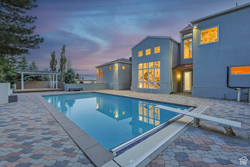 Pool at dusk featuring an outdoor pool, a patio area, a pergola, and a diving board