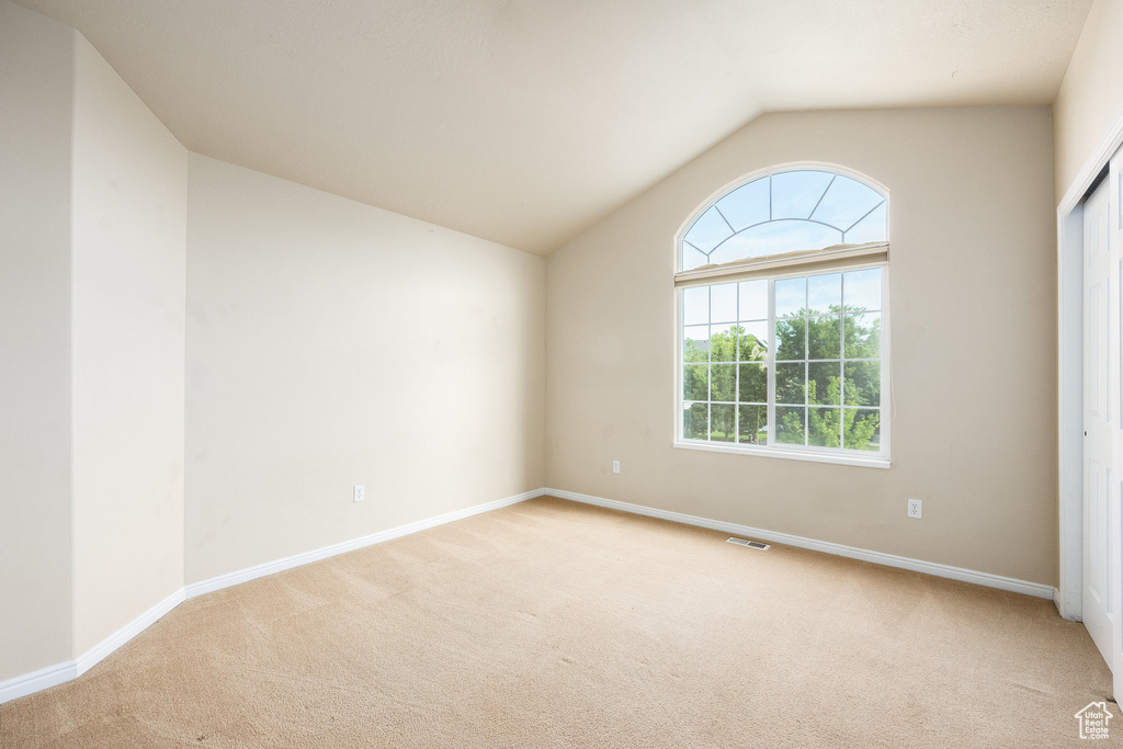 Carpeted empty room featuring lofted ceiling and baseboards