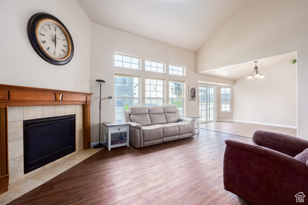 Living room featuring a tile fireplace, light wood-style floors, high vaulted ceiling, a chandelier, and baseboards