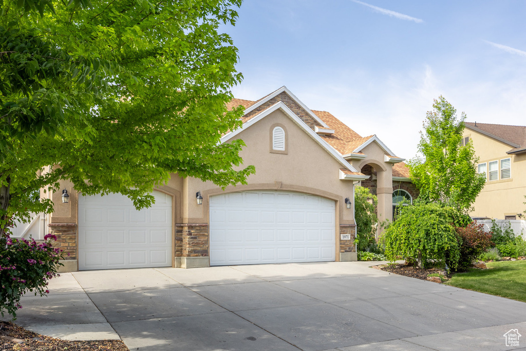 View of front facade with stone siding, stucco siding, driveway, and a garage