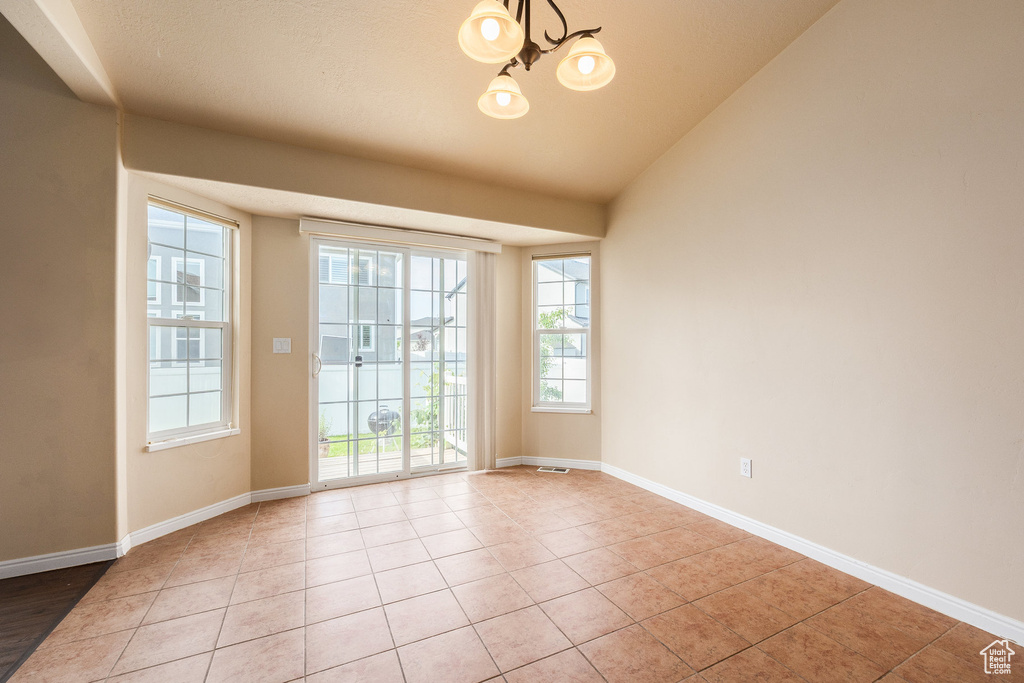Empty room featuring a chandelier, light tile patterned floors, baseboards, and lofted ceiling
