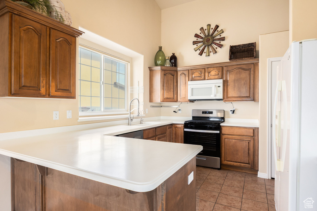 Kitchen featuring white appliances, a peninsula, a sink, light countertops, and light tile patterned floors