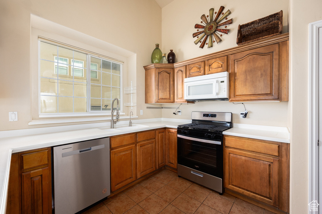 Kitchen featuring stainless steel appliances, a sink, dark tile patterned floors, brown cabinetry, and light countertops