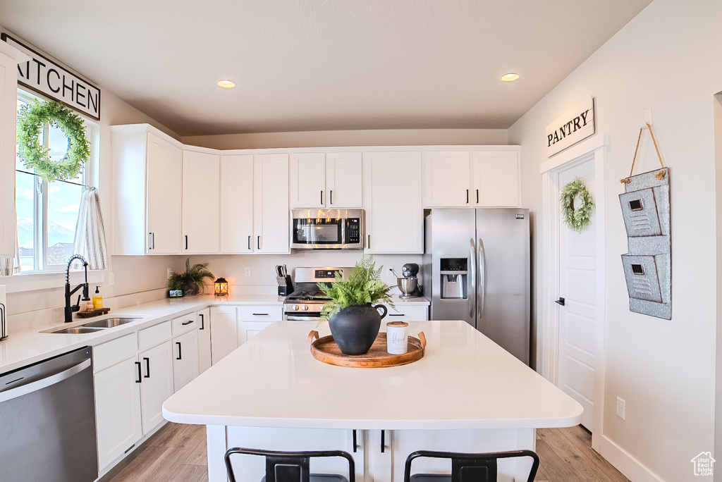 Kitchen with appliances with stainless steel finishes, a sink, light wood-type flooring, white cabinets, and recessed lighting