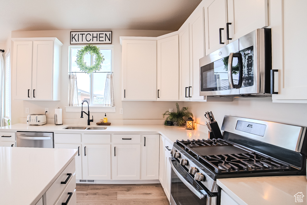 Kitchen featuring stainless steel appliances, a sink, light countertops, white cabinetry, and light wood finished floors