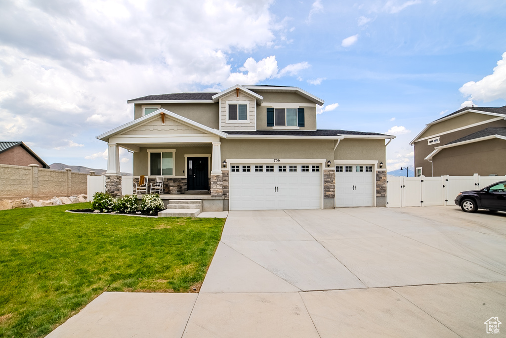 View of front of house featuring covered porch, stone siding, a gate, driveway, and a garage