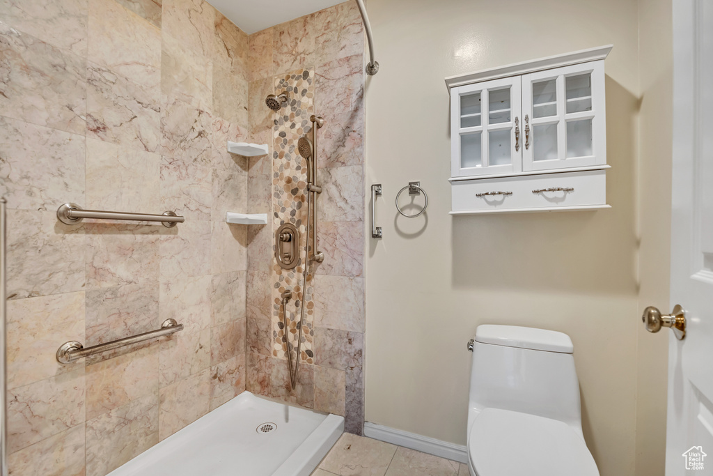 Full bathroom featuring tiled shower, toilet, tile patterned flooring, and baseboards