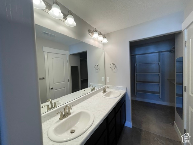Full bath with double vanity, a textured ceiling, and baseboards