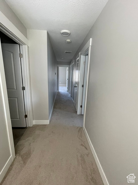 Corridor featuring light carpet, baseboards, and a textured ceiling