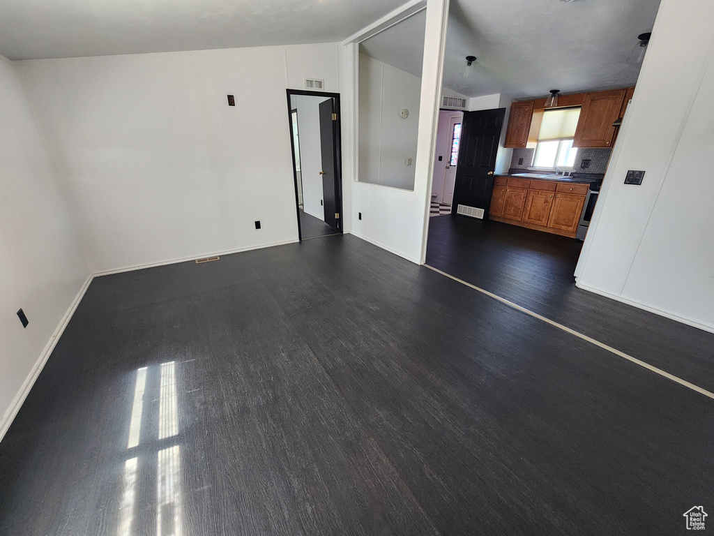 Unfurnished living room featuring dark wood finished floors, baseboards, and vaulted ceiling