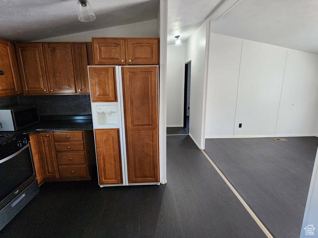 Kitchen with stainless steel range with gas stovetop, paneled refrigerator, brown cabinets, dark wood-style flooring, and vaulted ceiling