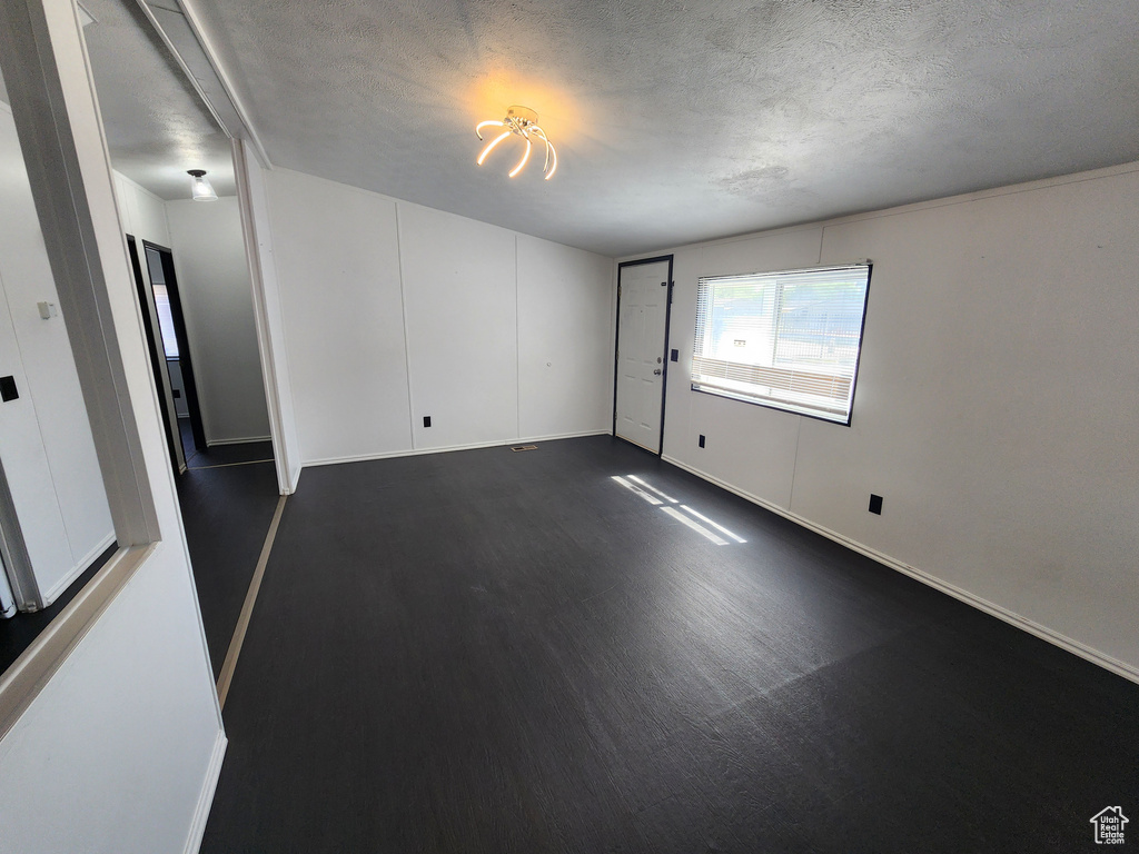 Empty room featuring a textured ceiling, baseboards, and dark wood finished floors