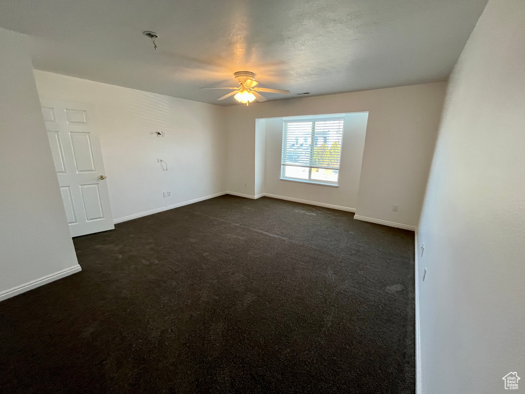 Spare room with ceiling fan, dark carpet, and baseboards