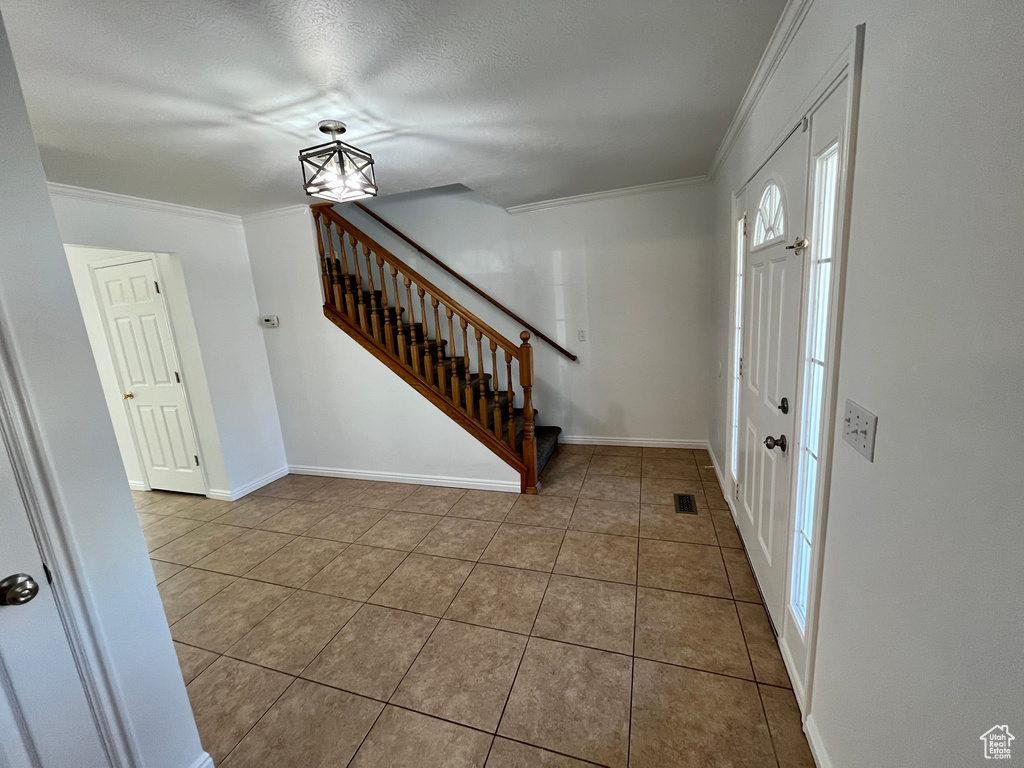 Tiled entryway with stairs, ornamental molding, and baseboards