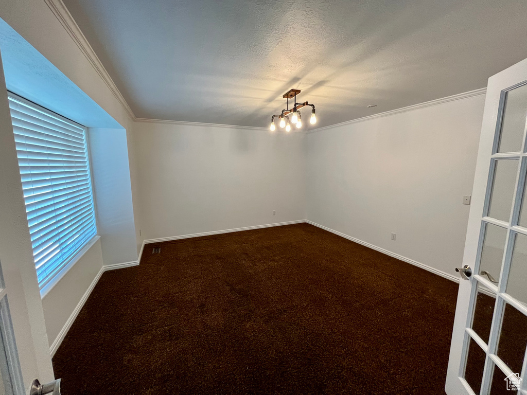 Empty room featuring dark carpet, crown molding, baseboards, and a chandelier