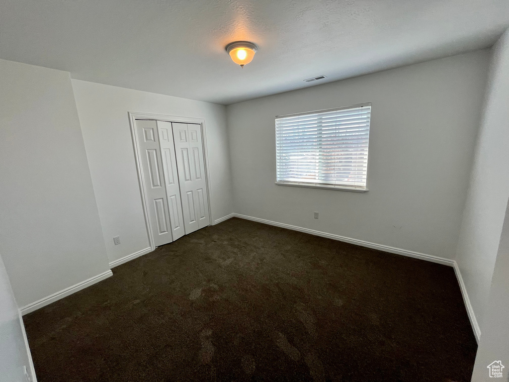 Unfurnished bedroom with dark carpet, a closet, and baseboards