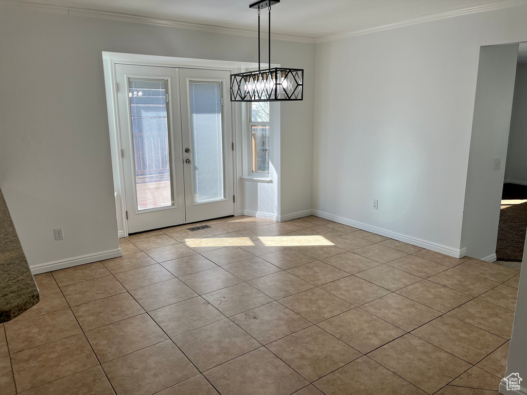 Unfurnished dining area featuring tile patterned flooring, crown molding, a chandelier, french doors, and baseboards