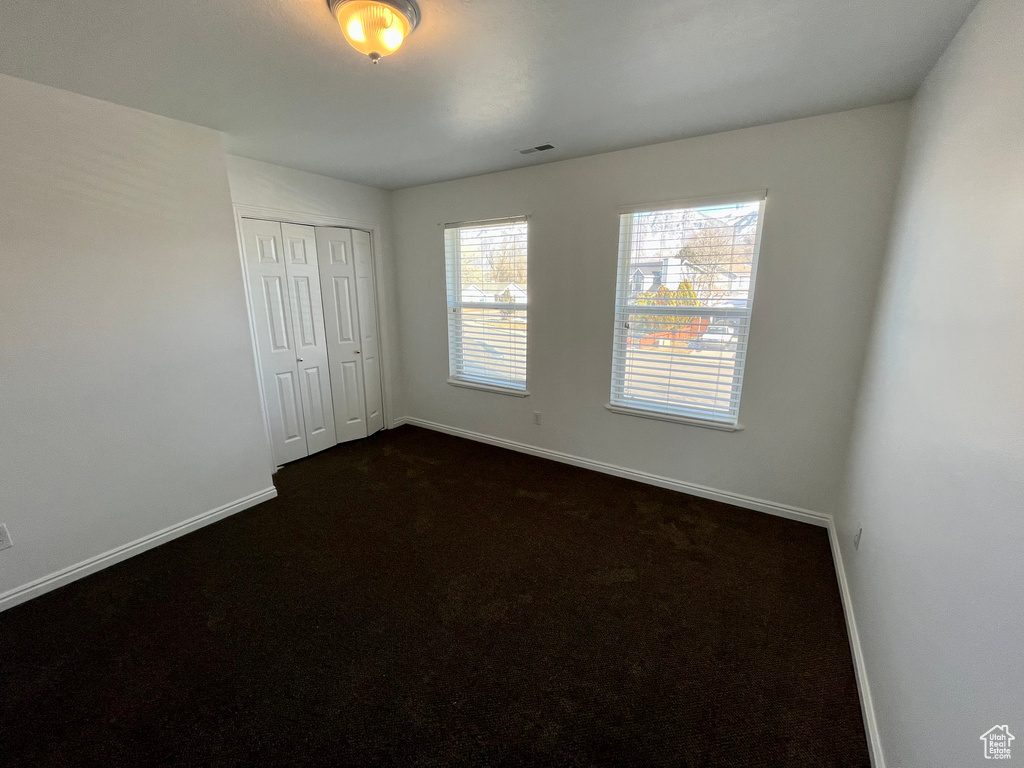 Unfurnished bedroom with baseboards, a closet, and dark carpet