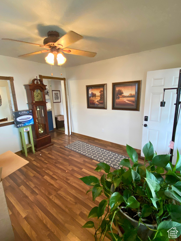 Living room featuring dark wood-type flooring, ceiling fan, and baseboards