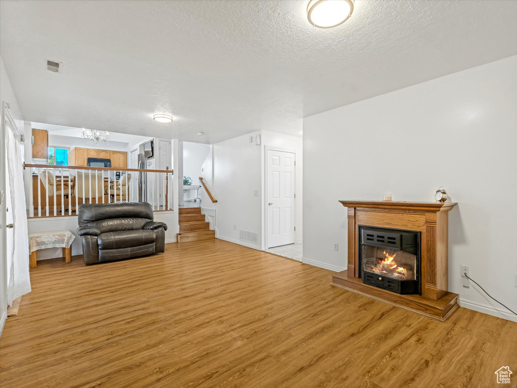 Living area featuring wood finished floors, stairway, a chandelier, a glass covered fireplace, and a textured ceiling