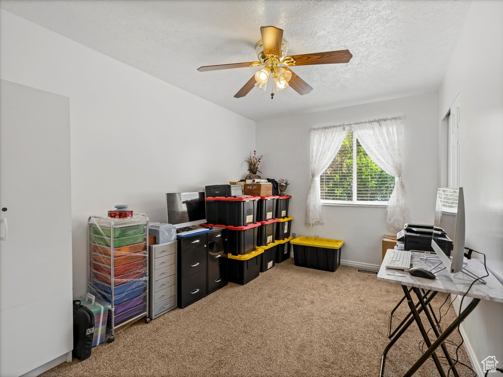 Carpeted home office featuring ceiling fan, baseboards, and a textured ceiling