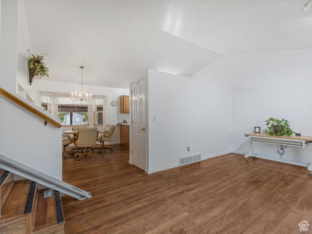 Living area with vaulted ceiling, wood finished floors, a chandelier, and stairs