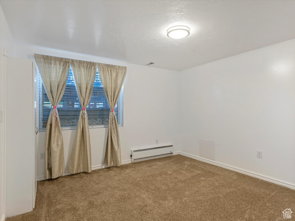 Carpeted empty room featuring a baseboard heating unit, baseboards, and a textured ceiling