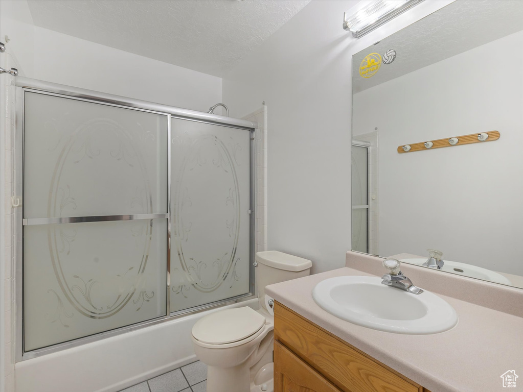 Full bath with vanity, tile patterned floors, toilet, and bath / shower combo with glass door