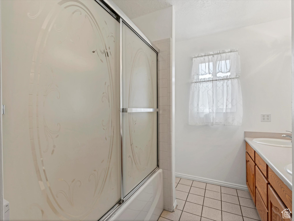 Bathroom featuring double vanity, combined bath / shower with glass door, tile patterned floors, and baseboards