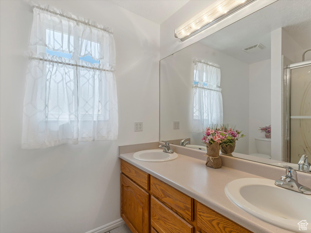 Full bathroom featuring plenty of natural light, double vanity, a shower stall, and toilet