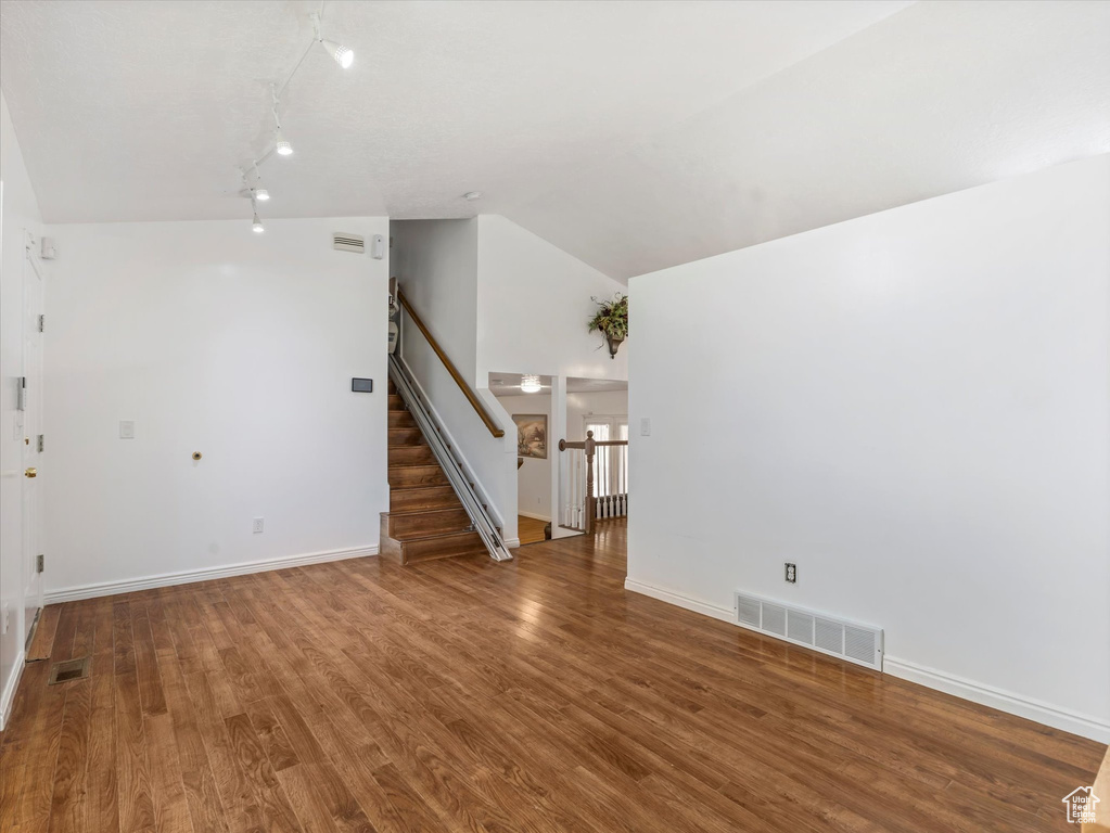 Unfurnished living room with wood finished floors, stairway, vaulted ceiling, and baseboards