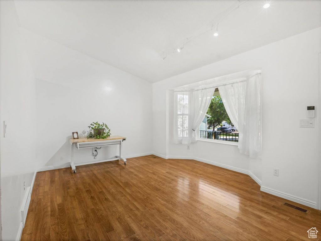 Unfurnished room with wood finished floors, baseboards, and rail lighting