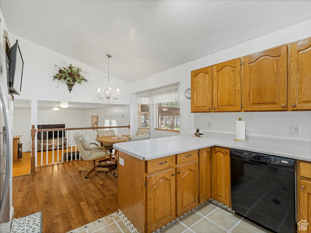 Kitchen with black dishwasher, a peninsula, light countertops, vaulted ceiling, and brown cabinets