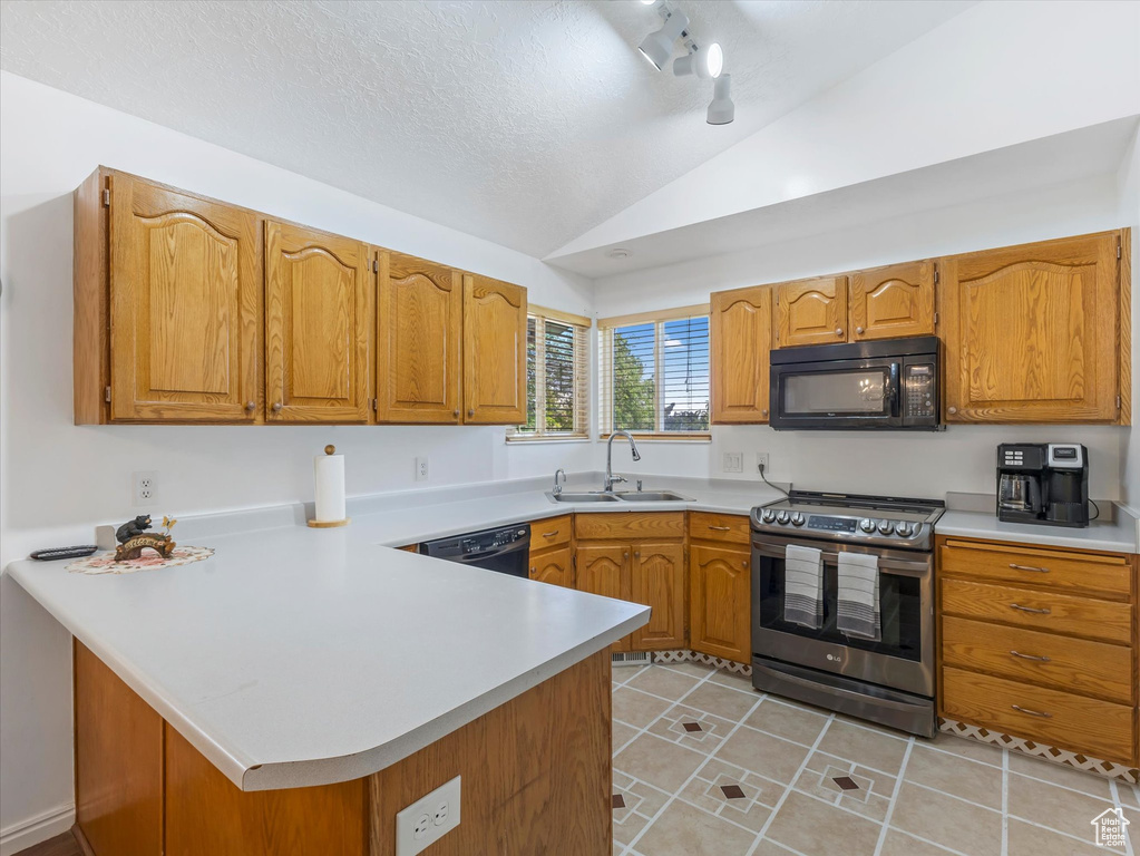 Kitchen with black appliances, a sink, vaulted ceiling, a peninsula, and light countertops