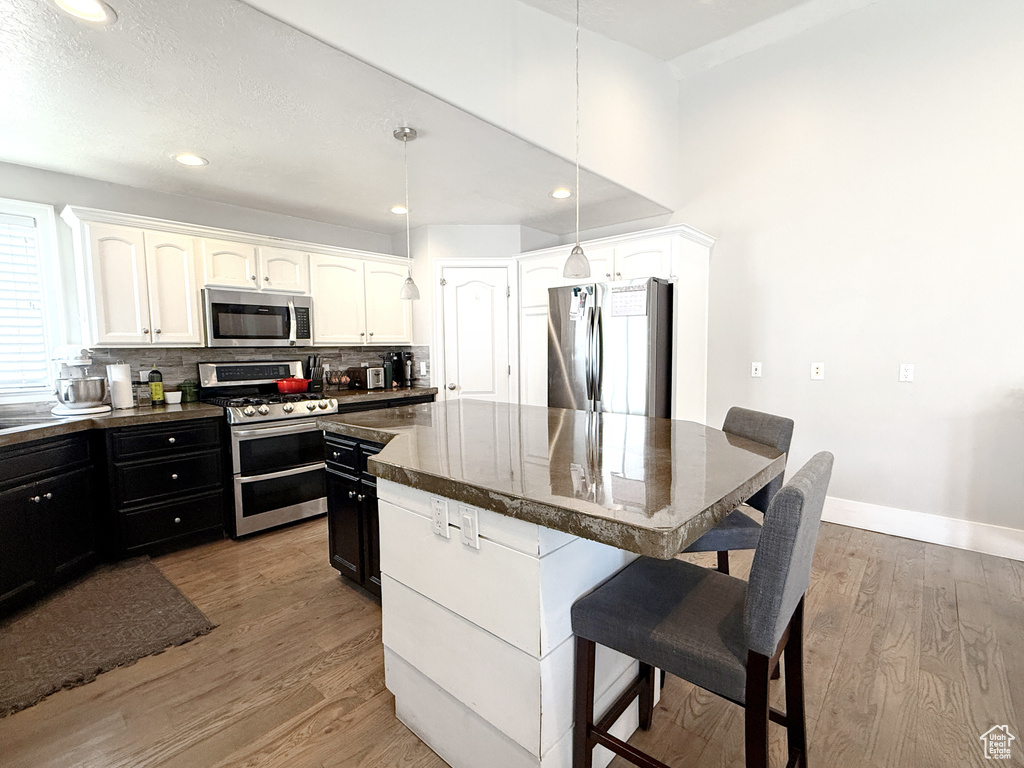 Kitchen featuring appliances with stainless steel finishes, a kitchen breakfast bar, a kitchen island, light wood-type flooring, and recessed lighting