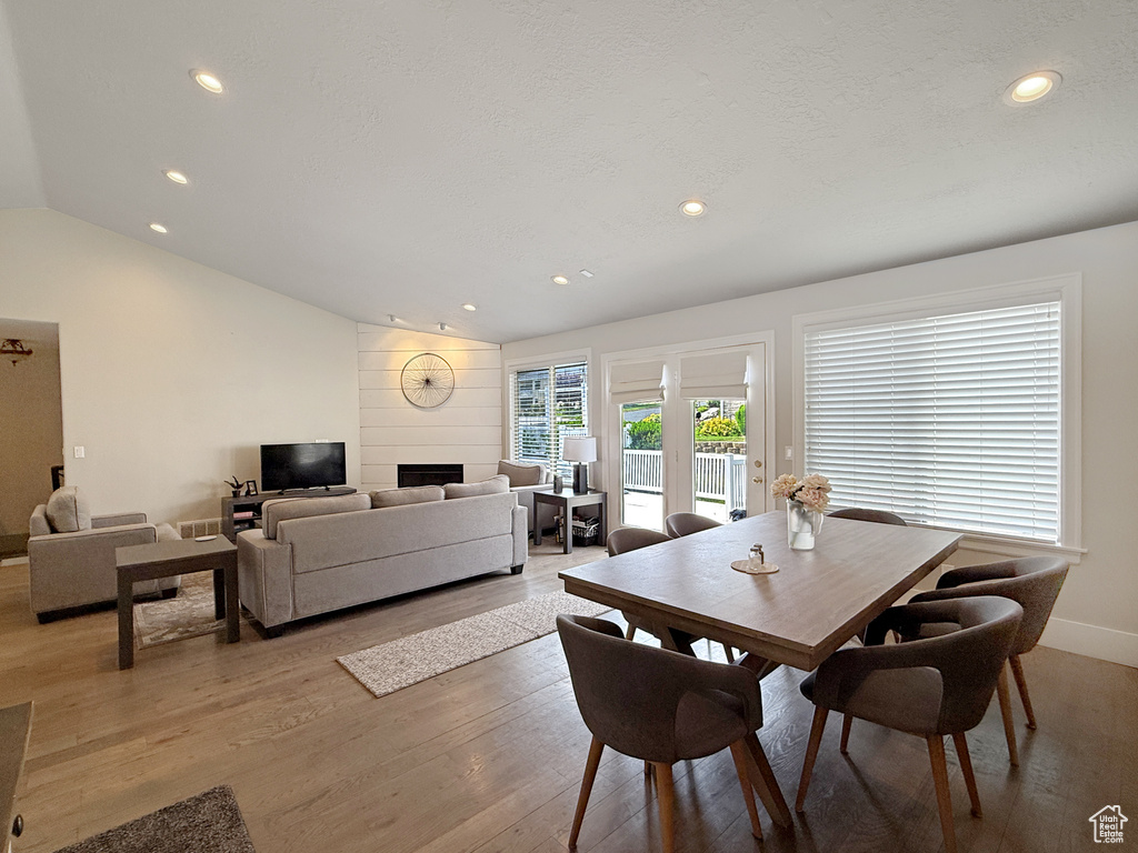 Dining space with vaulted ceiling, light wood-style flooring, recessed lighting, a large fireplace, and baseboards
