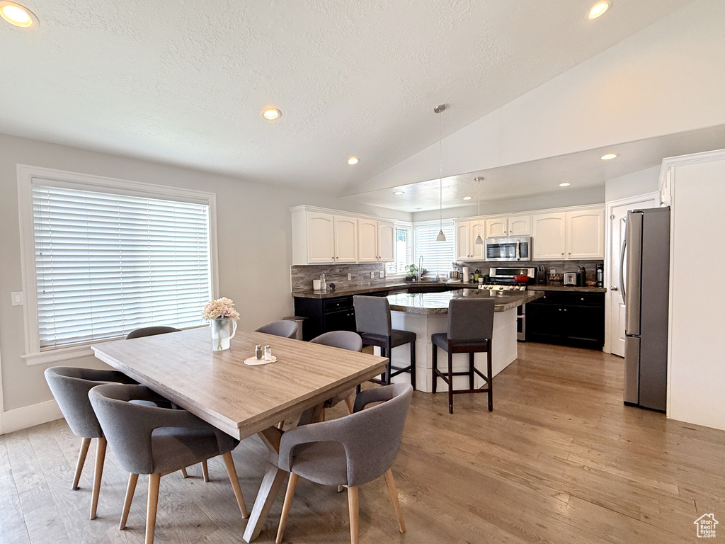 Dining room with light wood-style flooring, lofted ceiling, recessed lighting, a textured ceiling, and baseboards