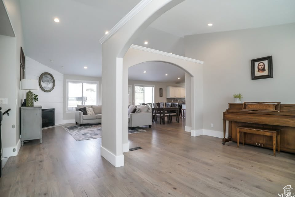 Living area featuring lofted ceiling, arched walkways, light wood-style floors, and baseboards
