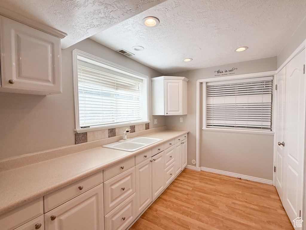 Kitchen with a sink, a textured ceiling, light countertops, light wood finished floors, and recessed lighting