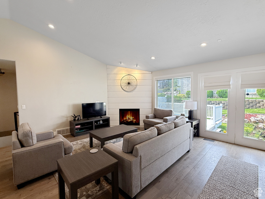 Living room featuring light wood-type flooring, lofted ceiling, a fireplace, and recessed lighting