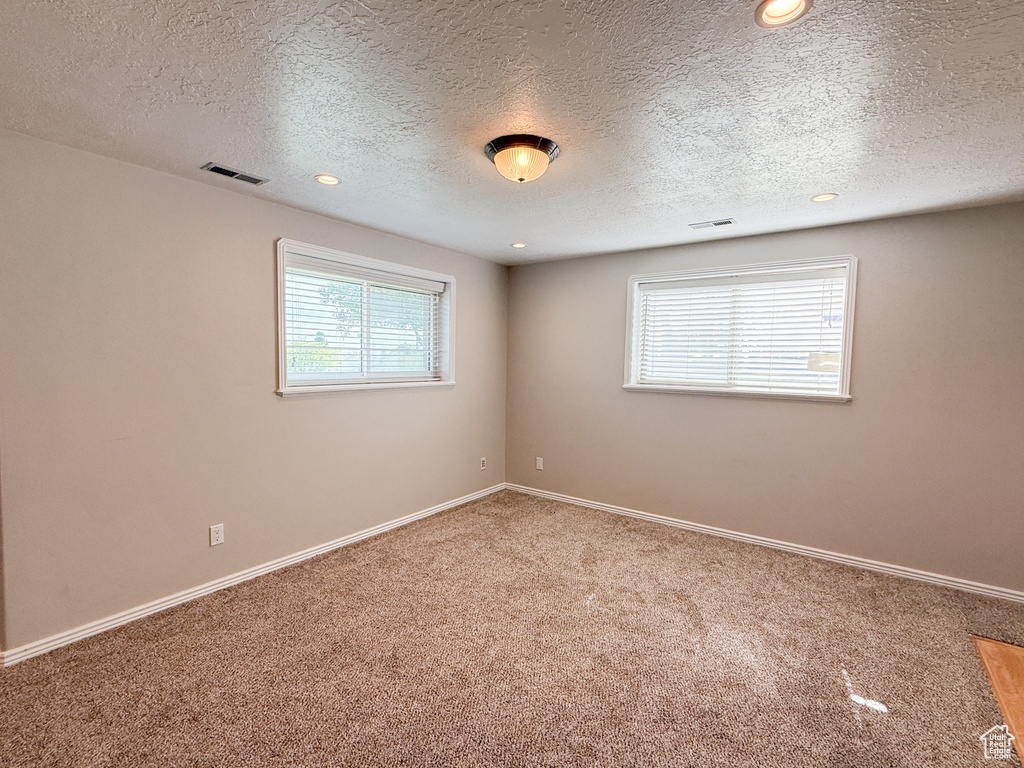 Carpeted empty room featuring a textured ceiling, recessed lighting, and baseboards