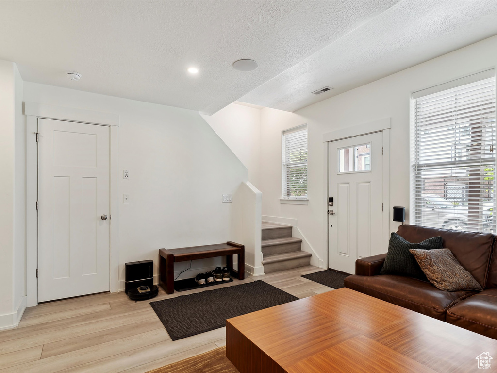 Living room featuring stairs, light wood-type flooring, a textured ceiling, baseboards, and recessed lighting