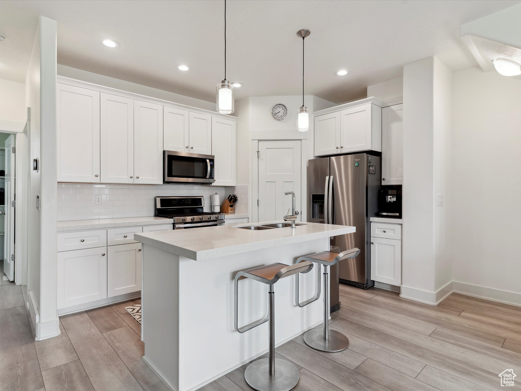 Kitchen with stainless steel appliances, a sink, light wood finished floors, white cabinetry, and light countertops