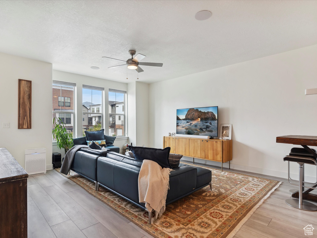 Living area featuring ceiling fan, light wood-style flooring, baseboards, and a textured ceiling