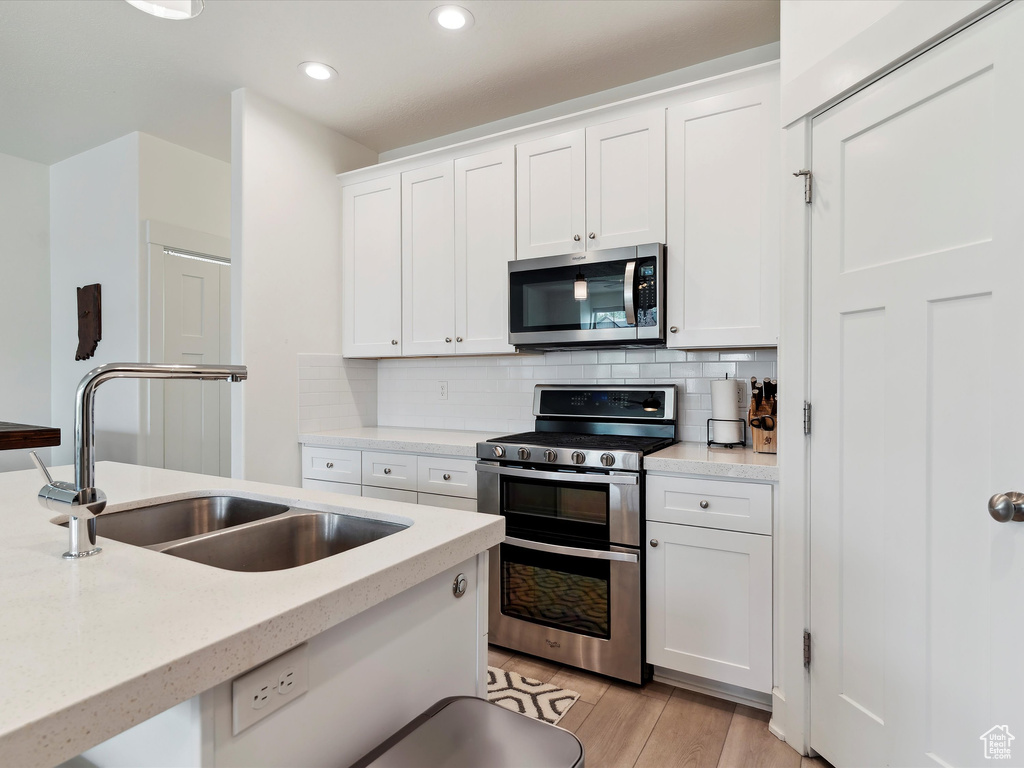Kitchen with stainless steel appliances, a sink, white cabinetry, backsplash, and recessed lighting