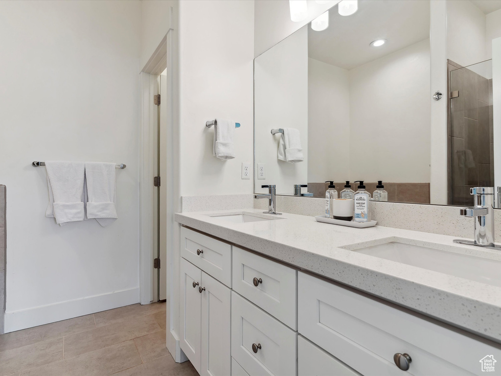 Full bath featuring double vanity, tiled shower, baseboards, and tile patterned floors
