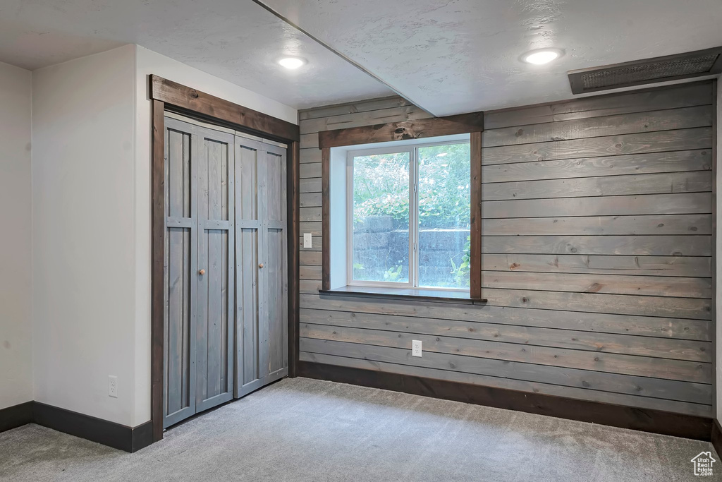 Unfurnished bedroom with baseboards, light colored carpet, wood walls, recessed lighting, and a closet
