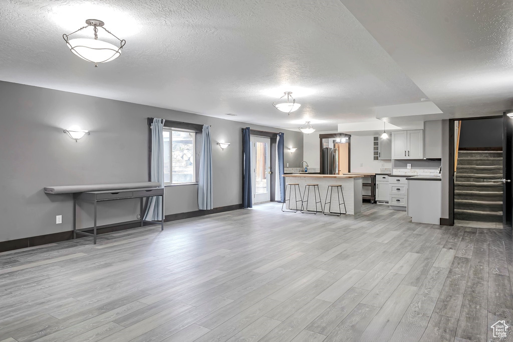 Unfurnished living room with a textured ceiling, light wood finished floors, baseboards, stairway, and a sink