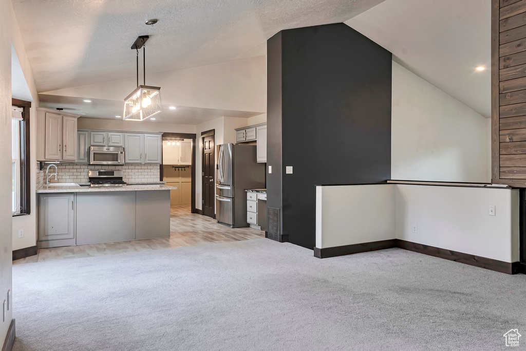Kitchen with appliances with stainless steel finishes, vaulted ceiling, light colored carpet, a peninsula, and light countertops